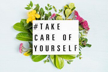 A positive self-care message surrounded by fresh flowers and leaves.