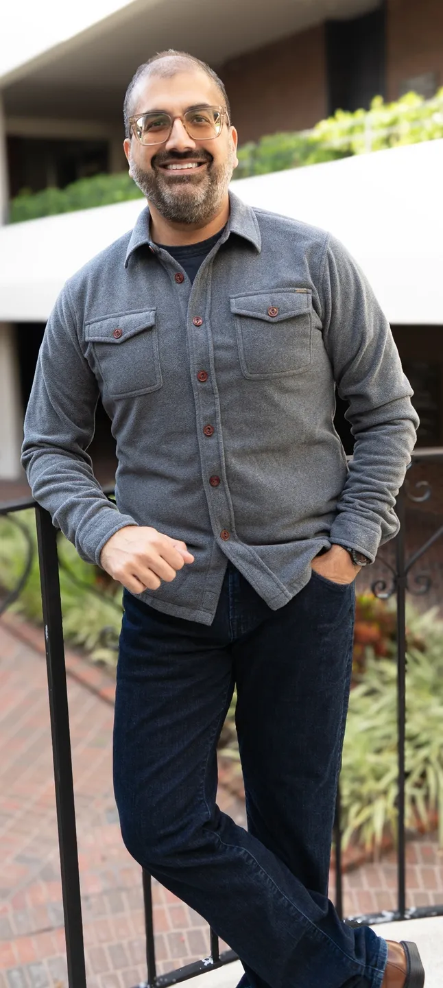 Man wearing a gray button-up shirt and black pants leaning on a railing.